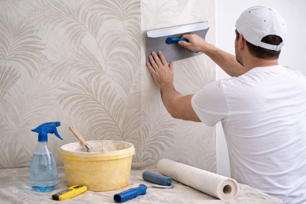 Stapsgewijs behang aanbrengen en met een behangspatel gladstrijken op de muur
